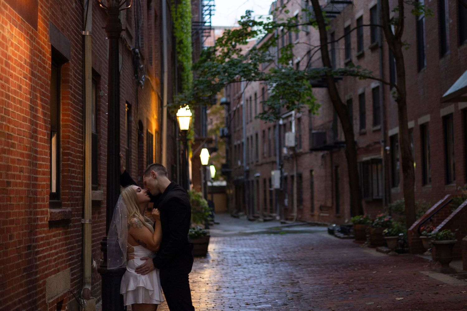 Romantic couple embraces on a charming cobblestone street in Boston's historic Beacon Hill neighborhood at dusk.