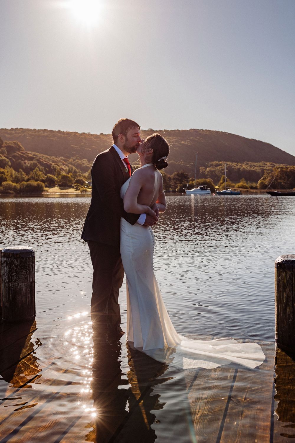Romantic couple shares tender moments at sunset on a lakeside dock with mountains in the background.