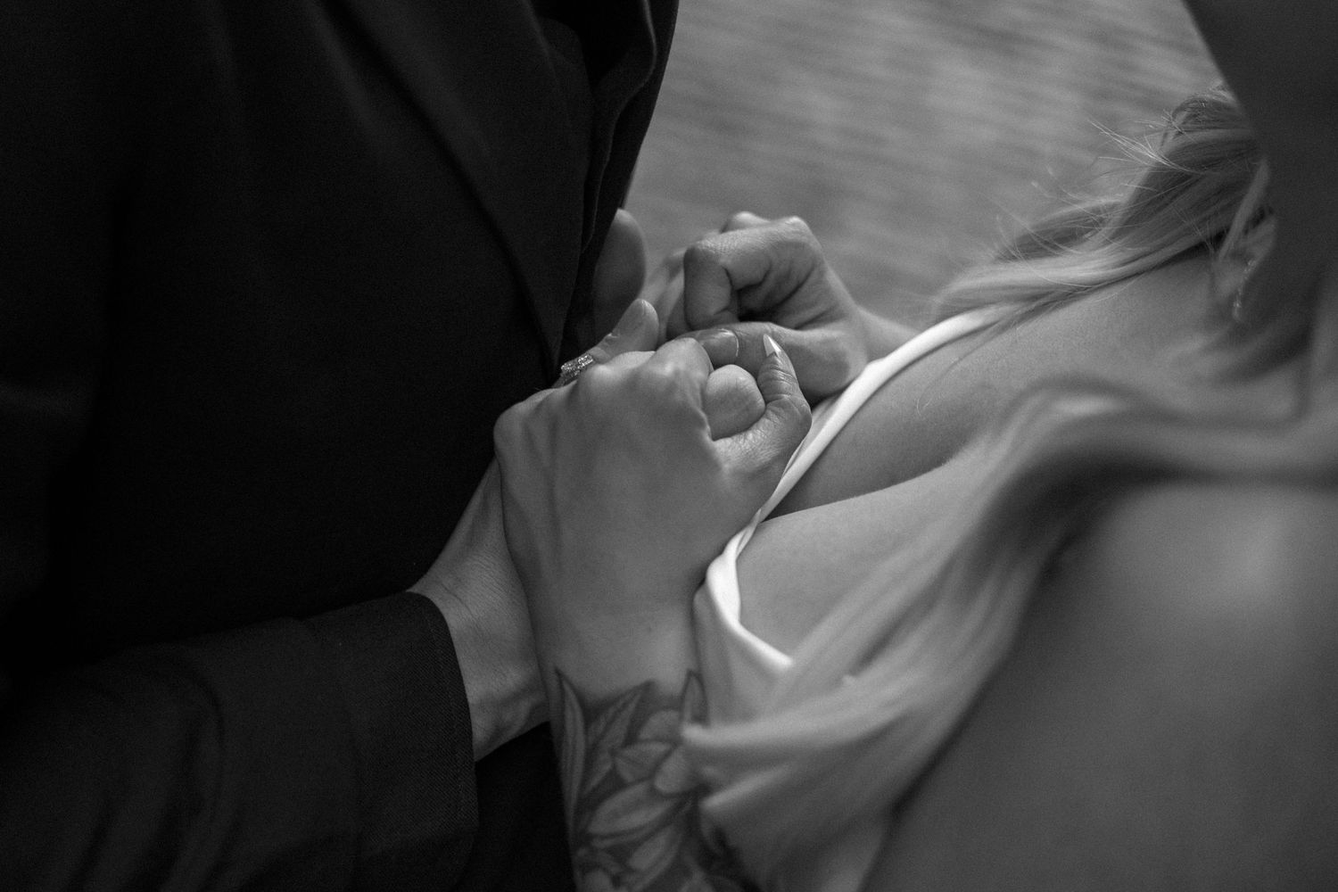 A black and white close-up photograph of hands clasped together in an intimate moment.