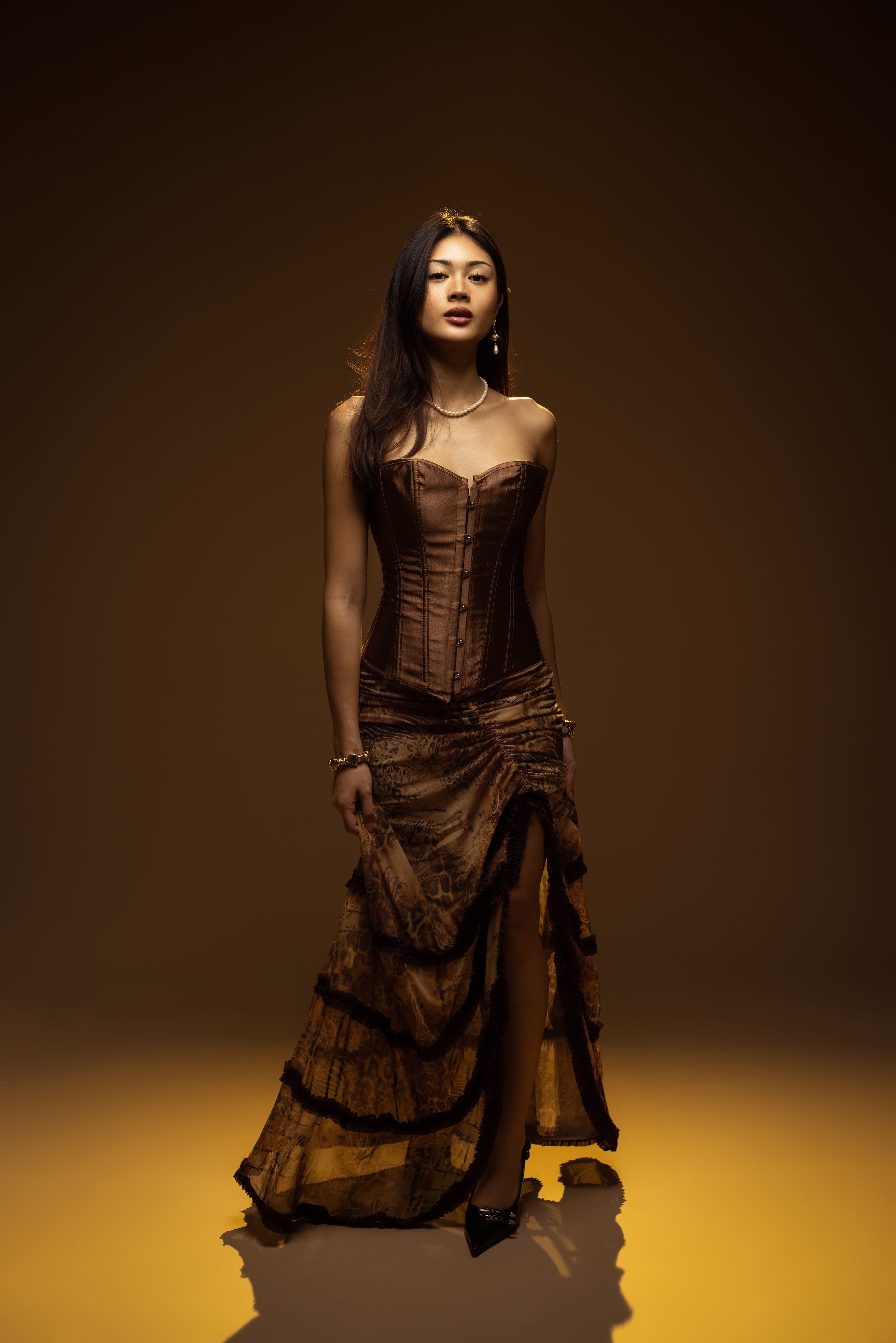 A dramatic fashion photo series showing a model in a brown corset dress against a dark background with yellow lighting.