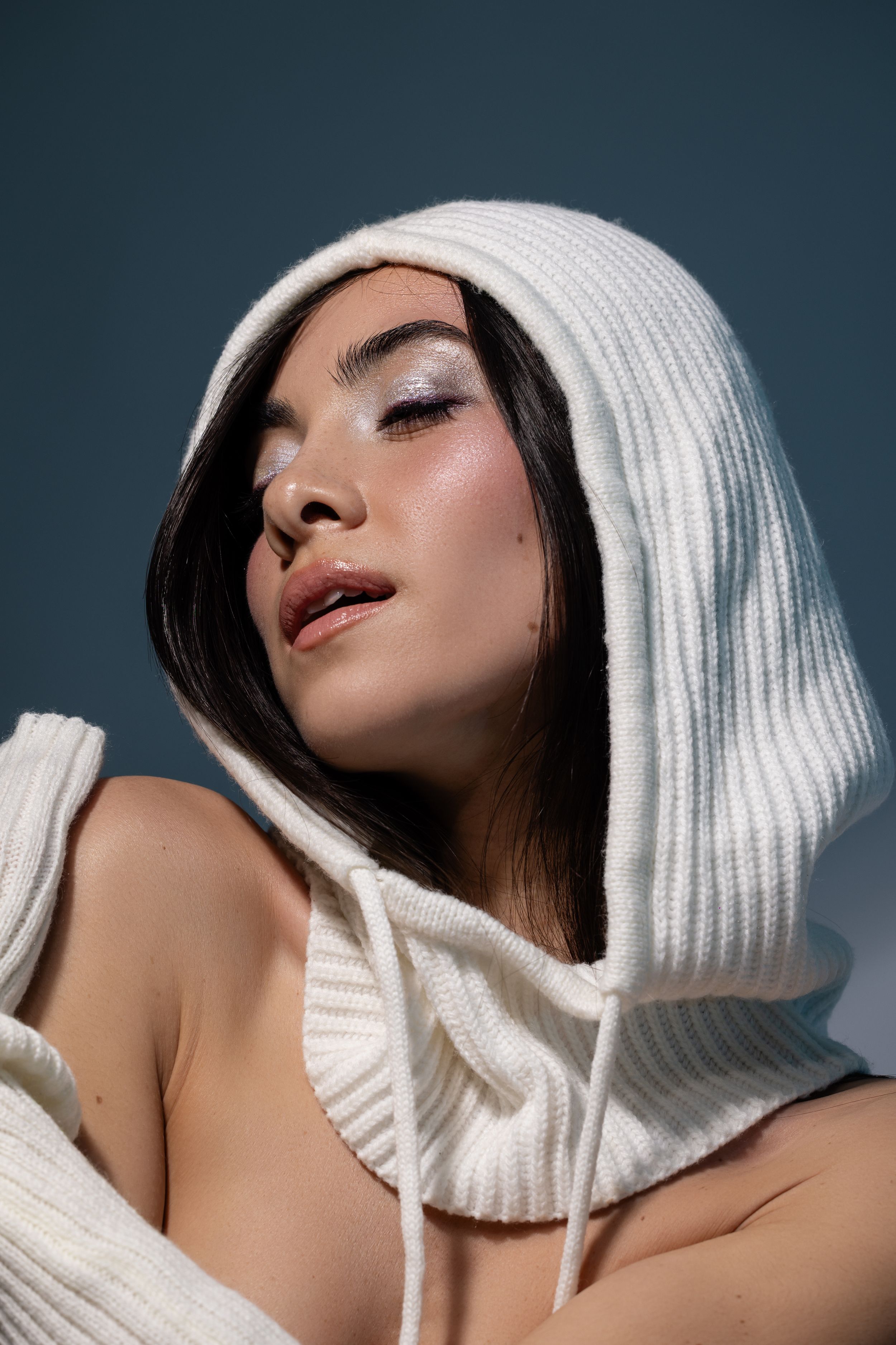 A fashion model poses in a white knit winter hat against a dark background in a series of artistic portraits.