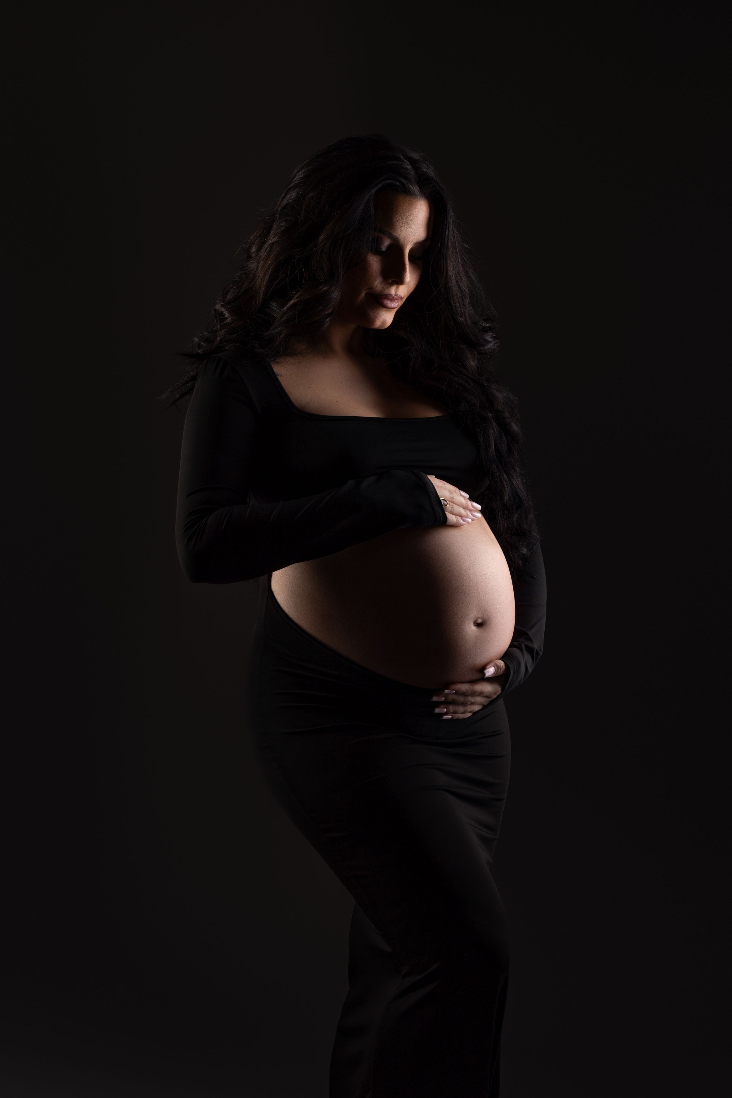 Silhouette of an expectant mother in a black dress against dark background, highlighting her pregnant belly.