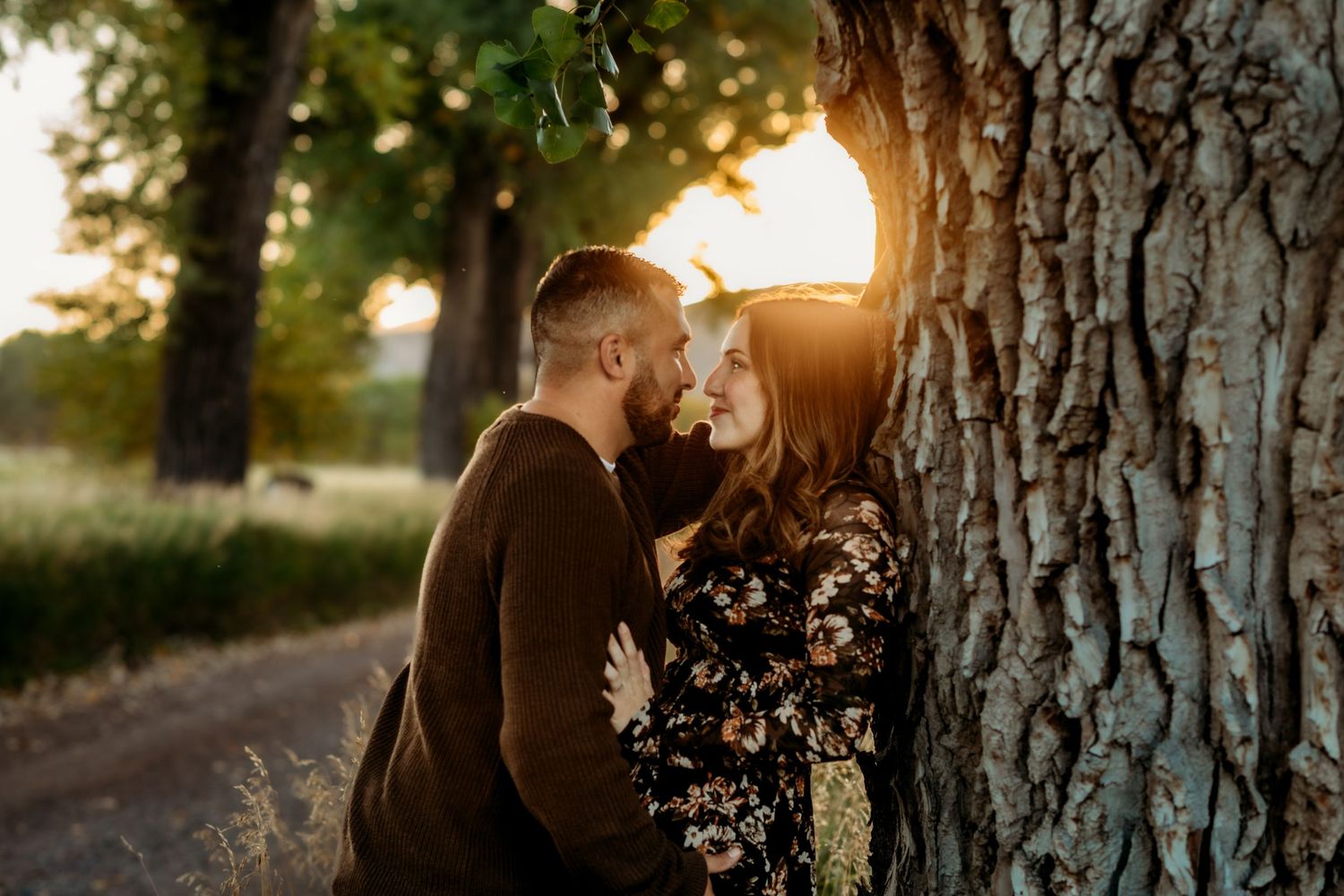 A couple embraces in silhouette against golden sunlight filtering through trees during a romantic outdoor photoshoot.