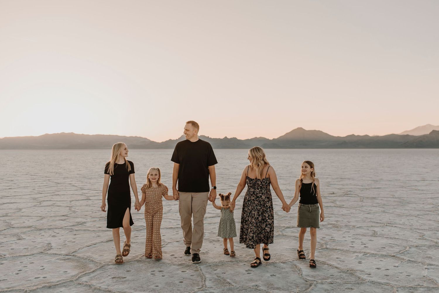 A family walks together on the Bonneville Salt Flats at sunset creating long shadows across the white landscape.