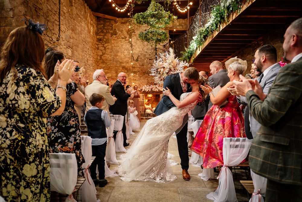 Guests celebrate during a wedding ceremony in a beautifully decorated stone barn venue.