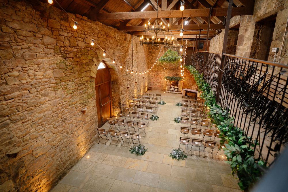 Empty chairs arranged for wedding ceremony in rustic stone barn with wooden beams. Doxford Barns