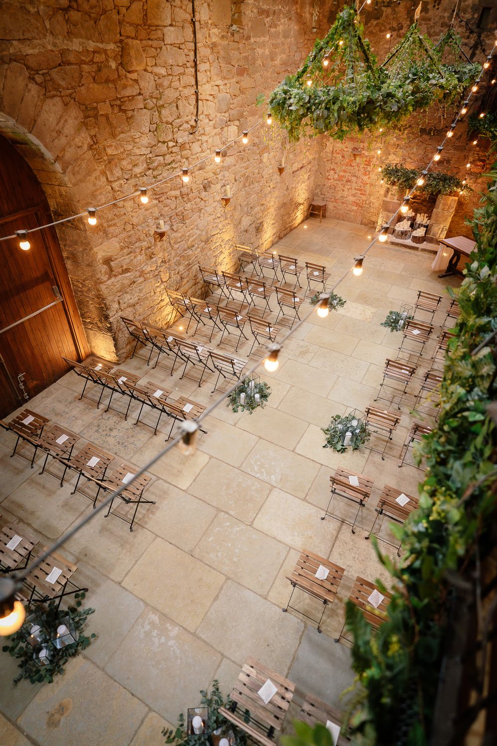 Overhead view of ceremony seating arrangement in stone venue with greenery and string lights. Doxford Barns
