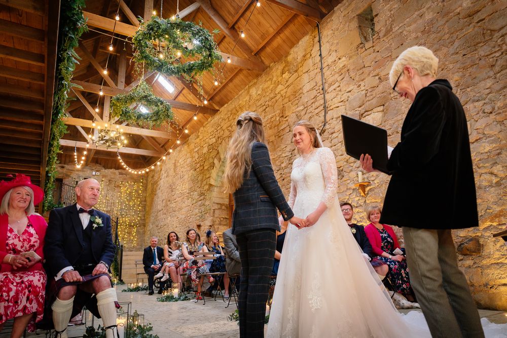Wedding ceremony taking place in historic stone barn with wooden beam ceiling.
