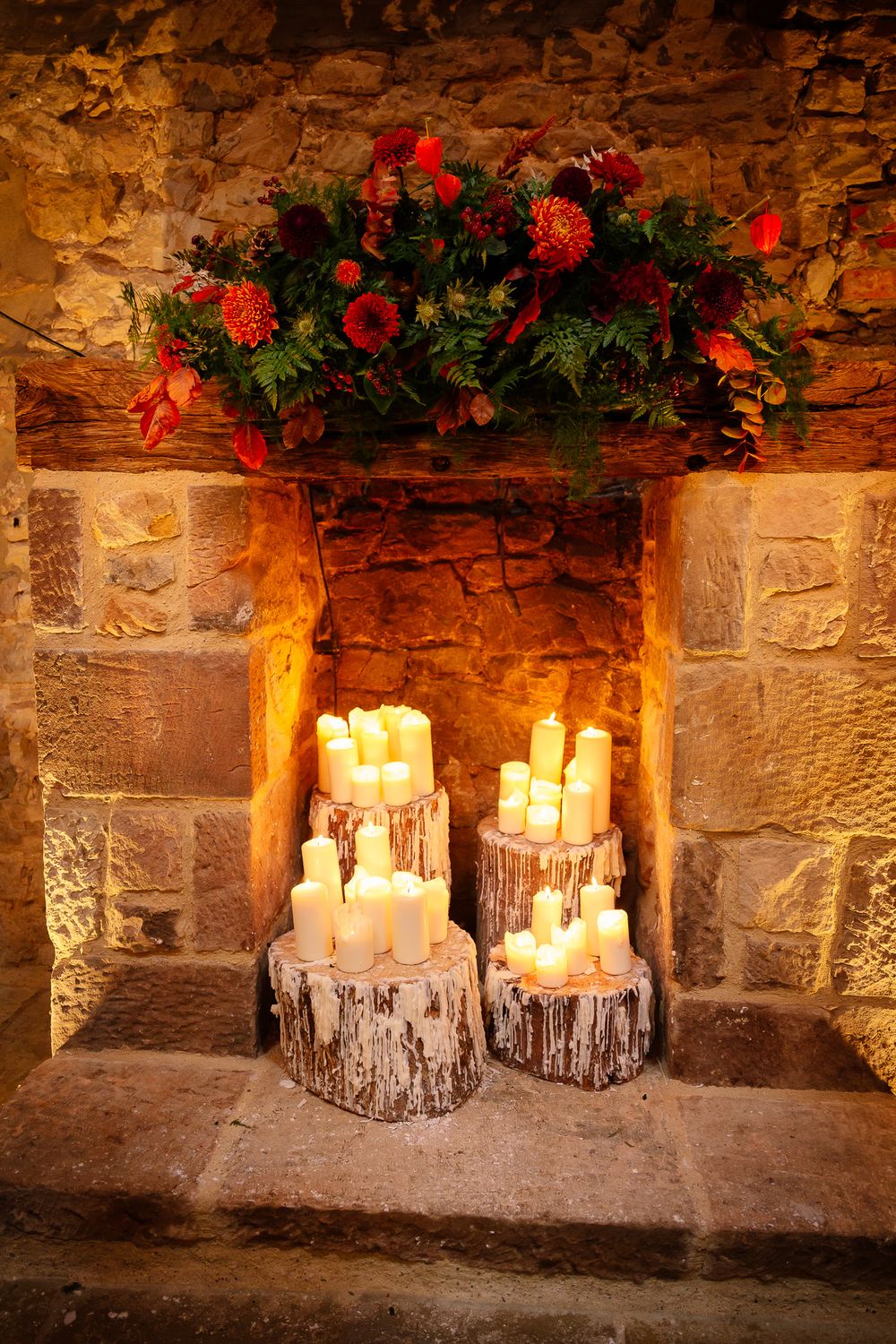 Romantic candle display with red floral arrangements on stone ledge in rustic venue.