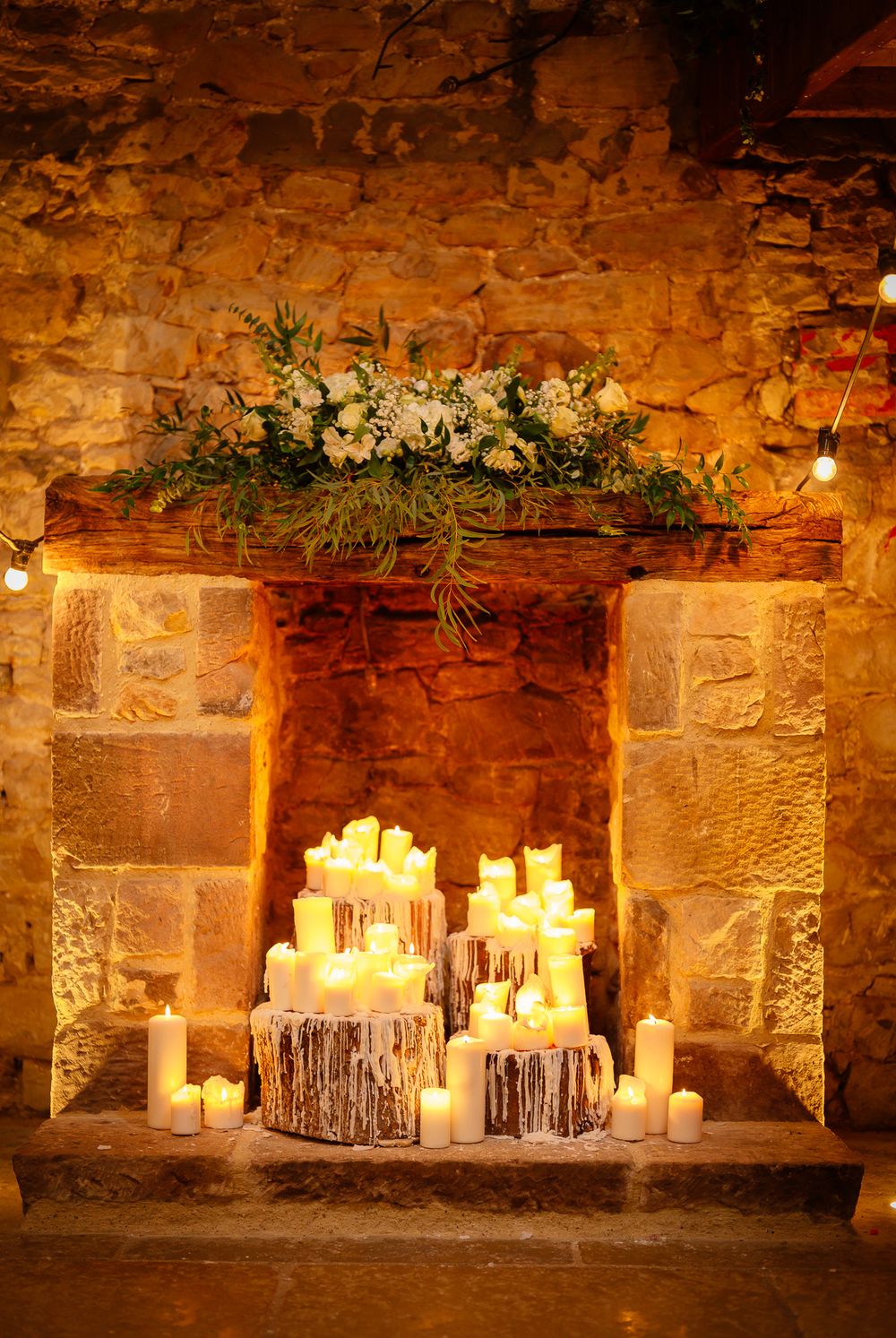 Elegant candle arrangement with floral decor against stone wall in wedding venue.