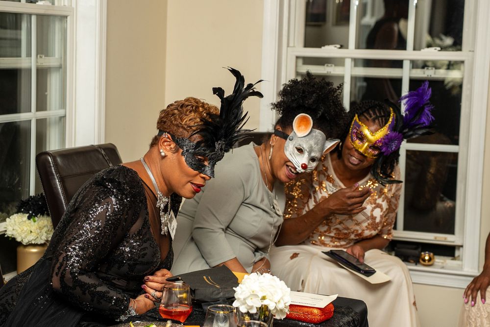 A group of people in formal attire sit at a table writing or signing documents together during an event.