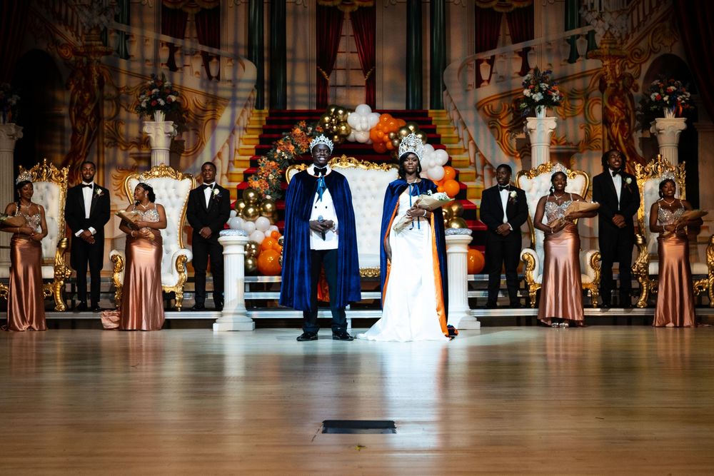 Dancers in elegant period costumes perform at a grand ballroom during a formal historical dance event.