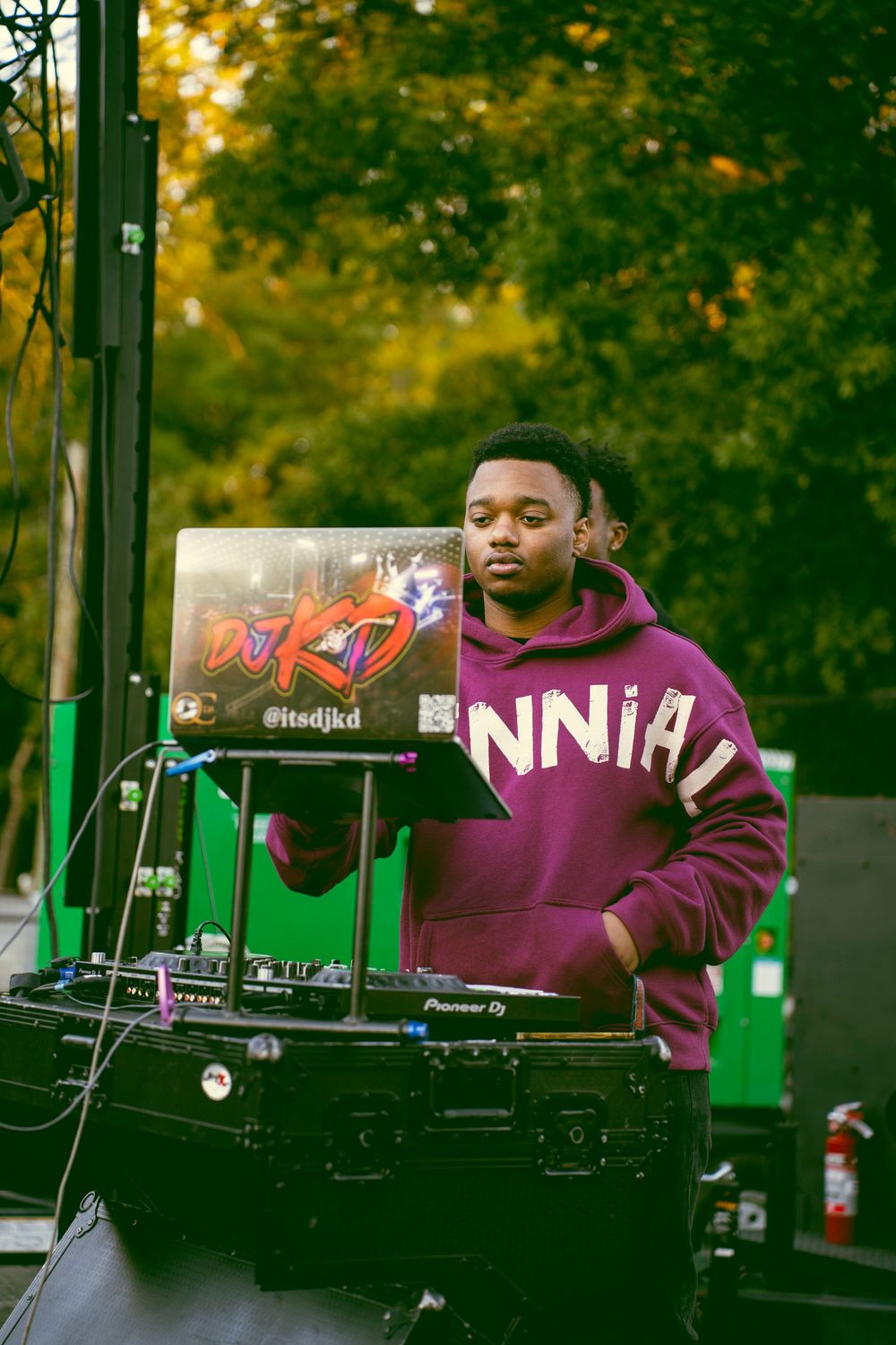DJ equipment and turntables set up outdoors with green trees in the background.