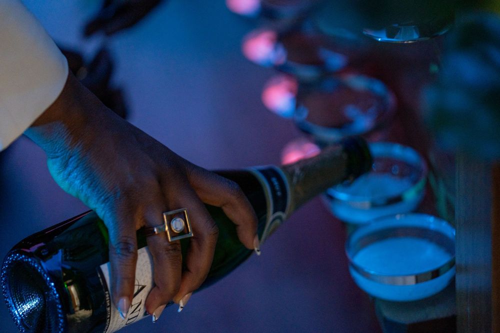 Close-up shot of hands preparing food on plates illuminated by dramatic blue and purple lighting.