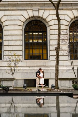 A couple sits together on a stone ledge outside a historic building with arched windows and classical architecture.