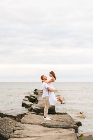 A romantic couple embraces on a rocky jetty overlooking the ocean during a cloudy day.