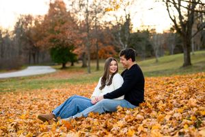 A couple enjoys a romantic autumn moment lying together in colorful fallen leaves during sunset.