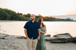 A couple shares a romantic moment at sunset by the water's edge with mountains in the background.