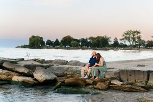 Couple sits together on large coastal rocks during sunset at a serene beach location.