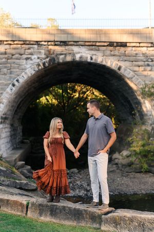 A couple stands together by a stone bridge archway during a golden sunset photo session.