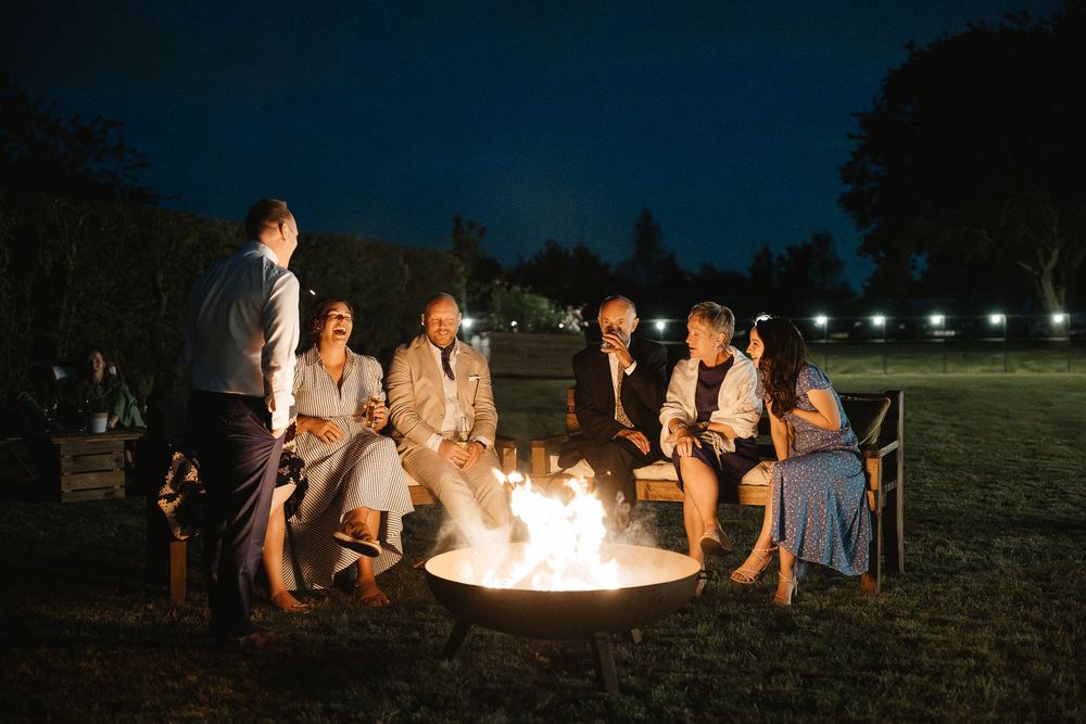 People gather around a glowing fire pit on a lawn at dusk, creating a cozy outdoor evening atmosphere.
