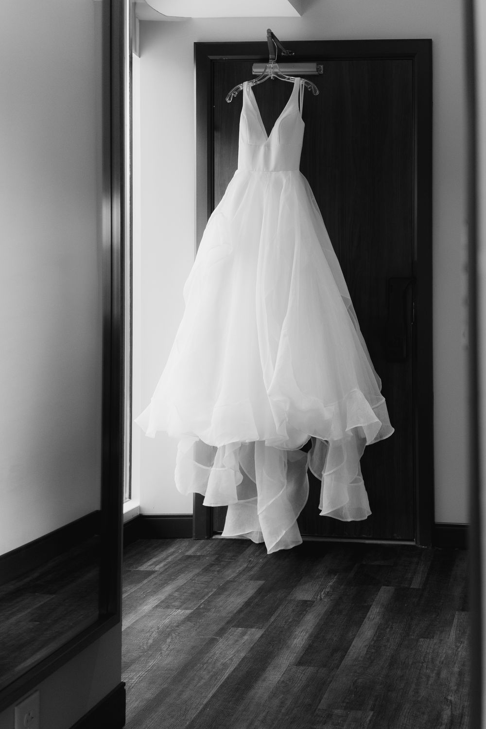 A black and white photo series showing a flowing white wedding dress hanging in dark doorways against hardwood floors.