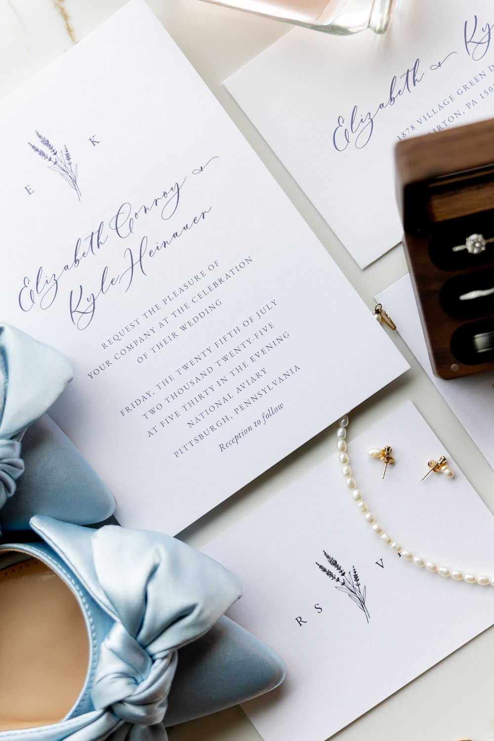 Elegant wedding invitations with pale blue silk bow and pearl details arranged on white background.