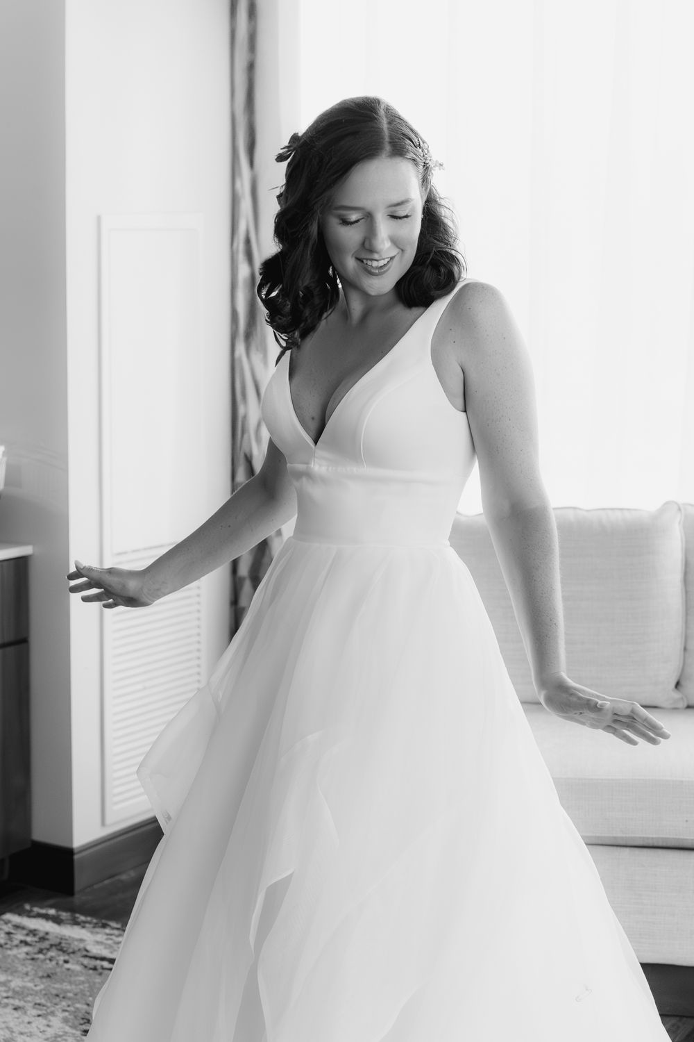 A bride in a flowing white wedding gown twirls gracefully in a bright sunlit room with white walls.