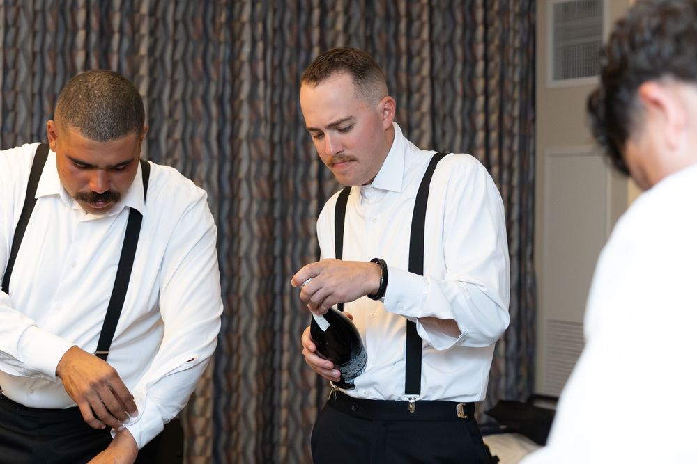 Two men in white dress shirts and suspenders getting ready for a formal event while adjusting their attire.