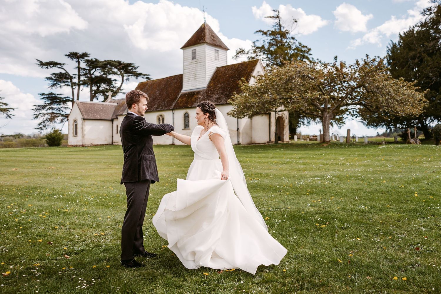 A couple shares a romantic moment on a grassy lawn with a white church steeple in the background.