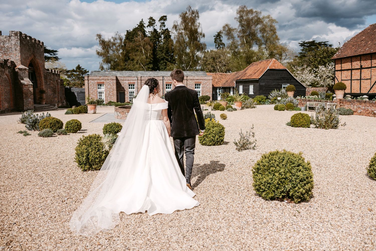 A panoramic view of a wedding ceremony setting with gravel paths and manicured shrubs under dramatic cloudy skies.