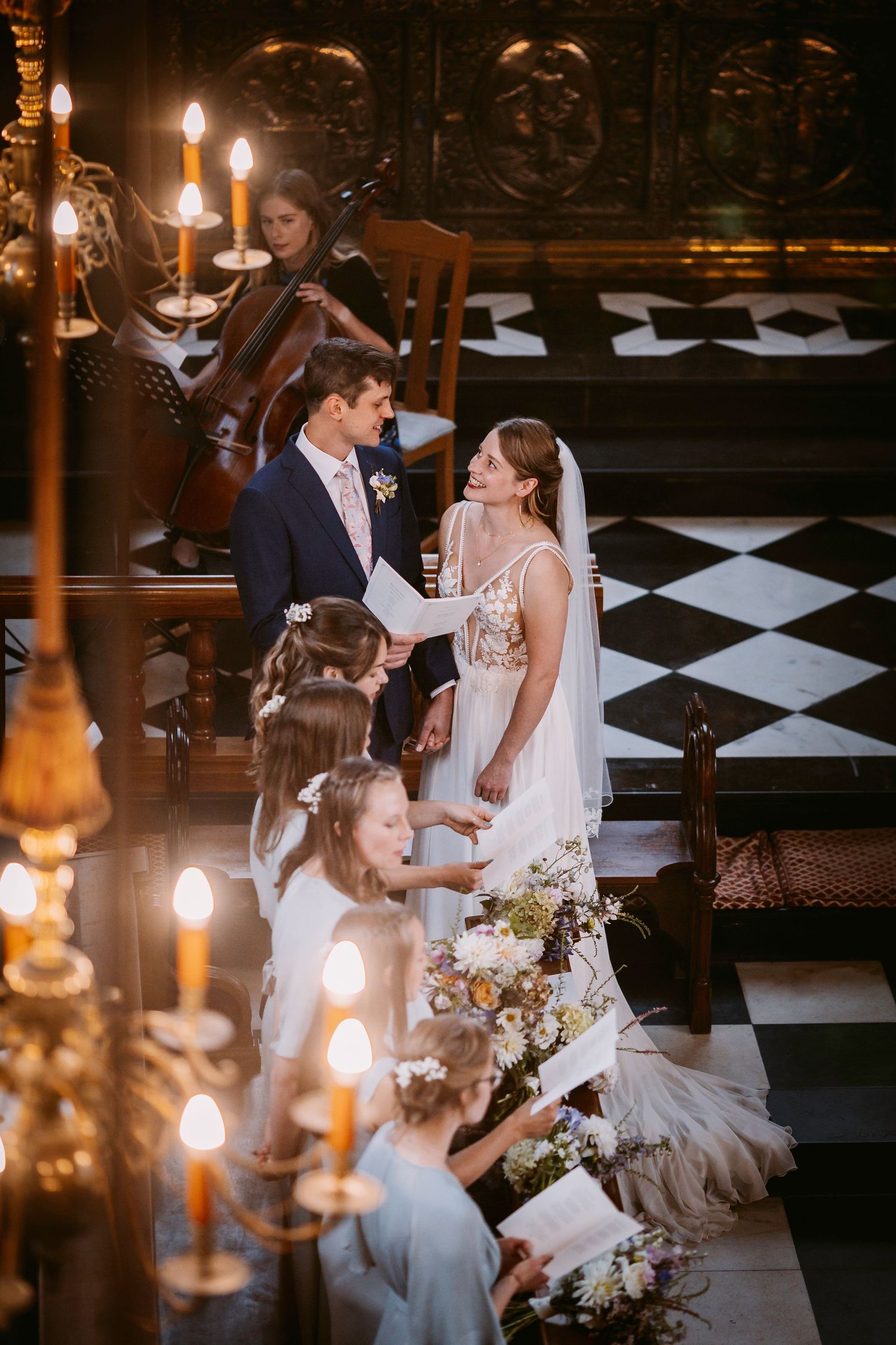 Newlyweds share intimate moments in a candlelit church interior with black and white checkered floor.