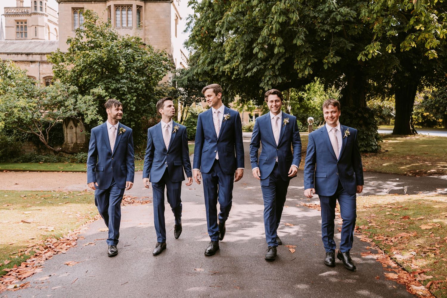 Groomsmen in navy suits walking together on a path during a wedding celebration.