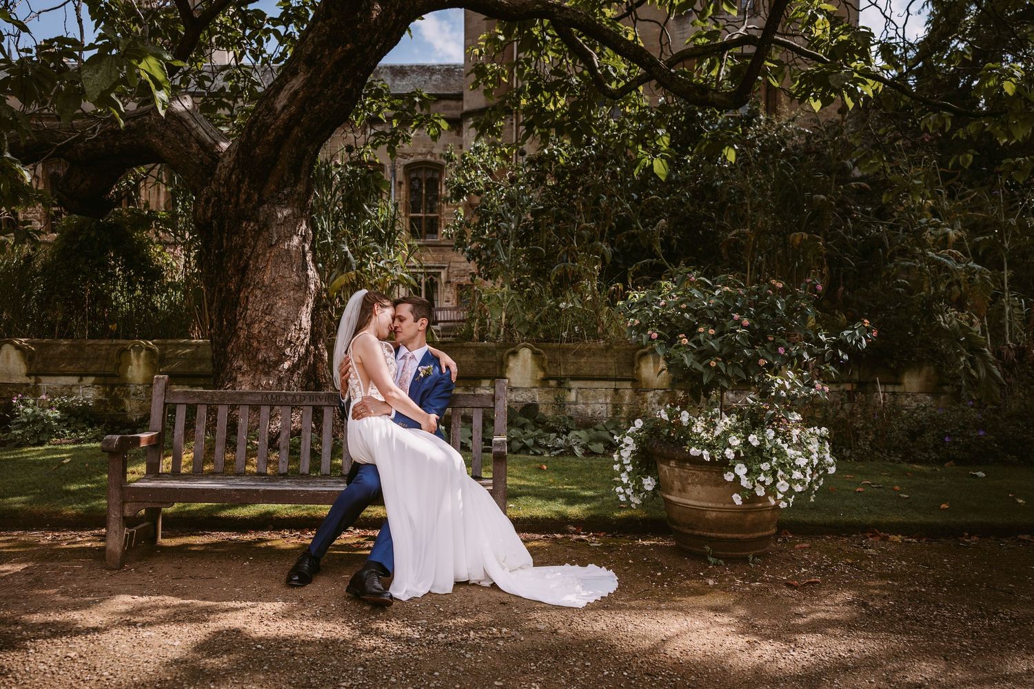 A couple shares a romantic moment together on a wooden bench in a lush garden setting during a sunny day.
