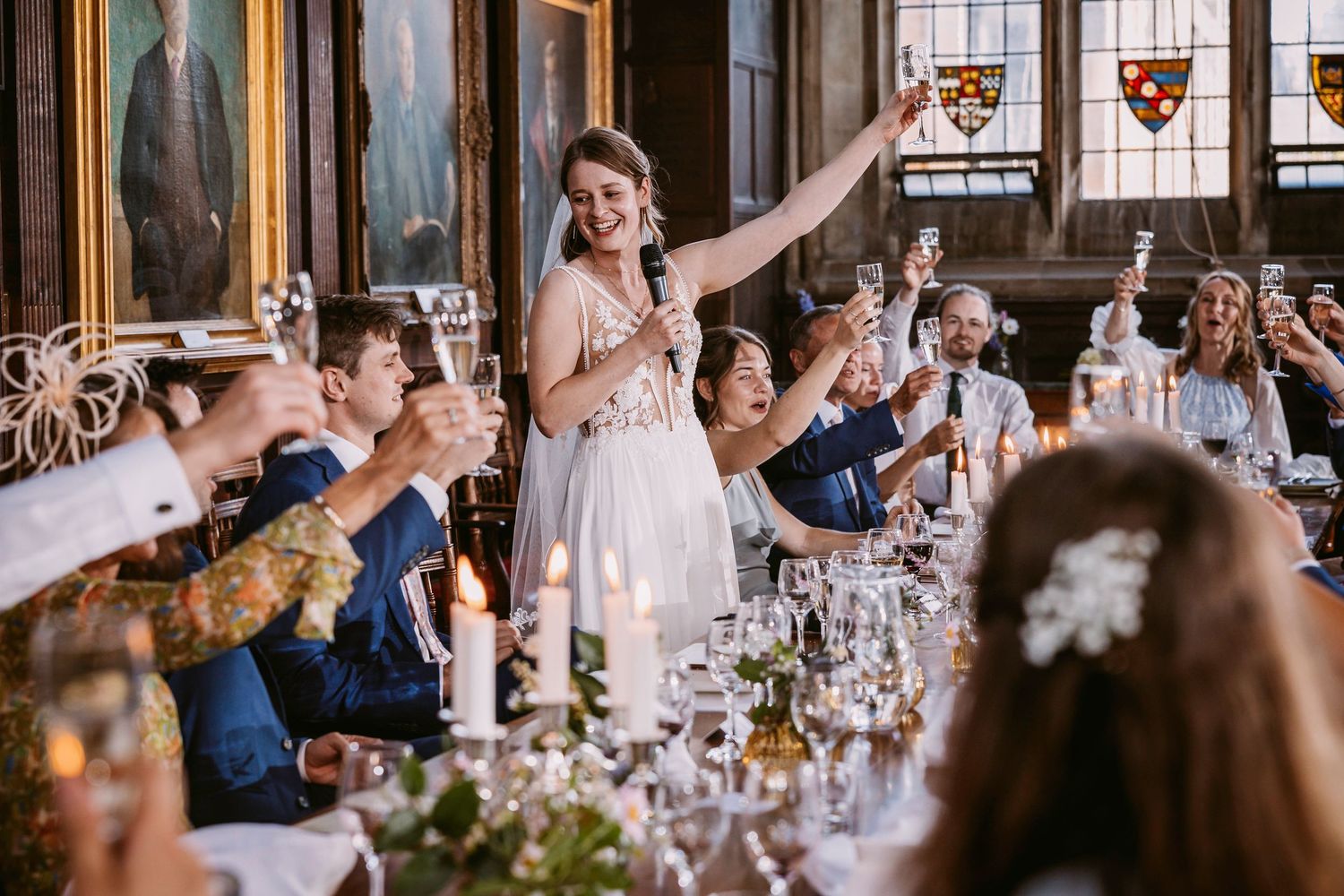 Wedding reception guests raising glasses in celebration at an elegant indoor venue with ornate decor.