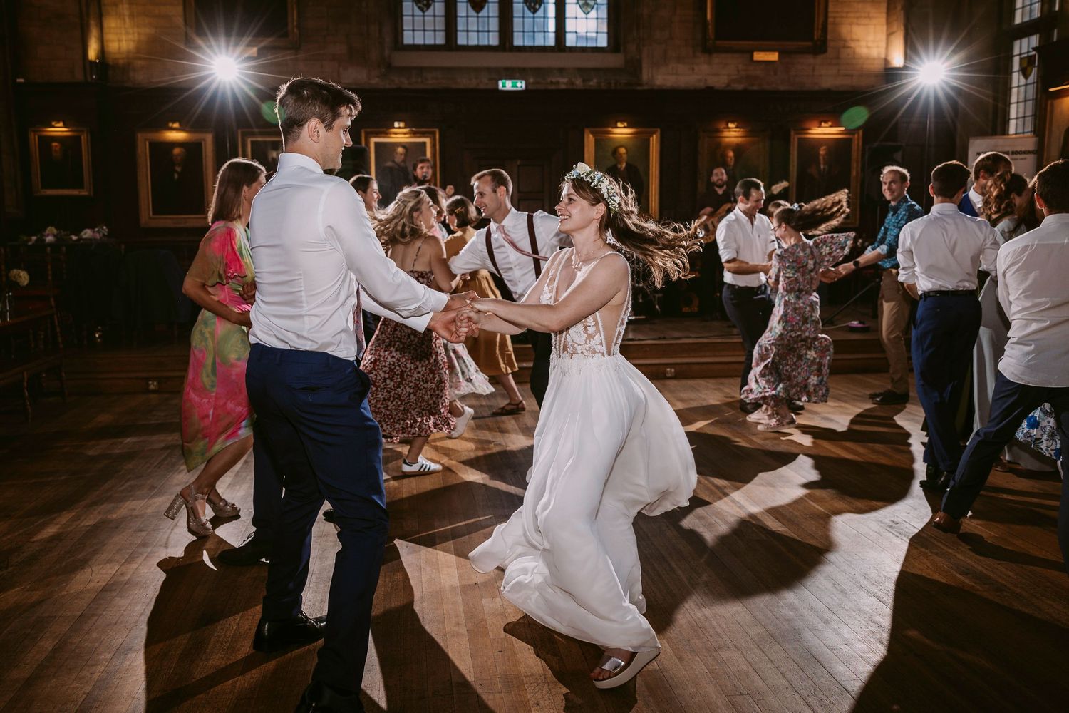 Wedding guests dance and twirl on a wooden dance floor during an evening reception celebration.