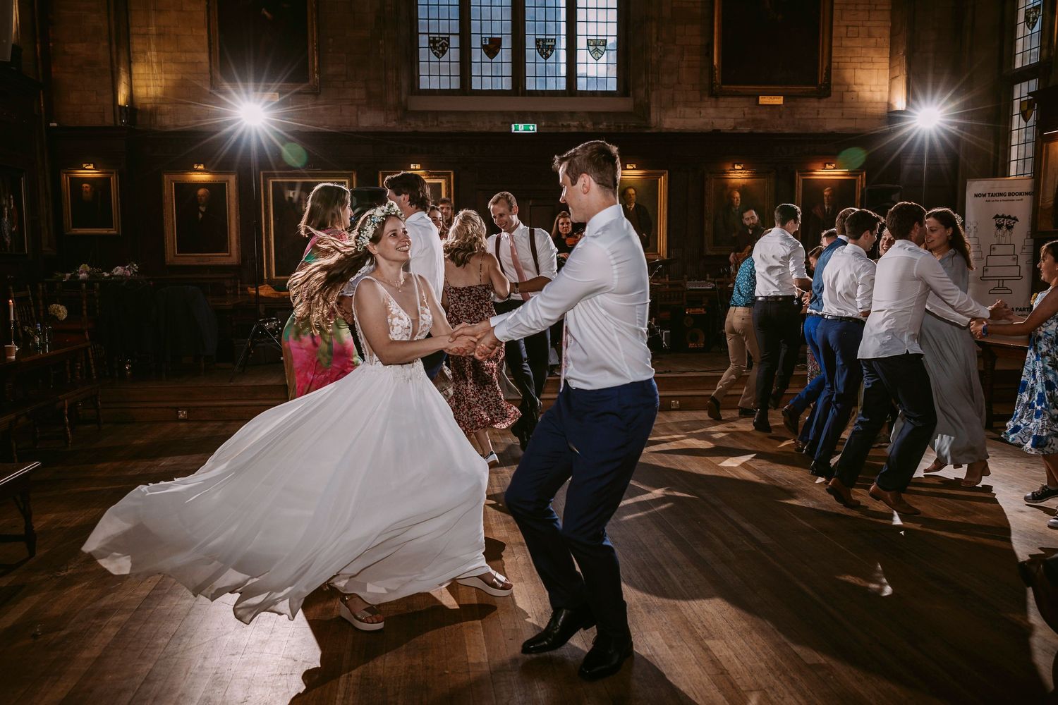 Wedding guests dance and celebrate on a dark wooden dance floor in an elegant venue with warm lighting.