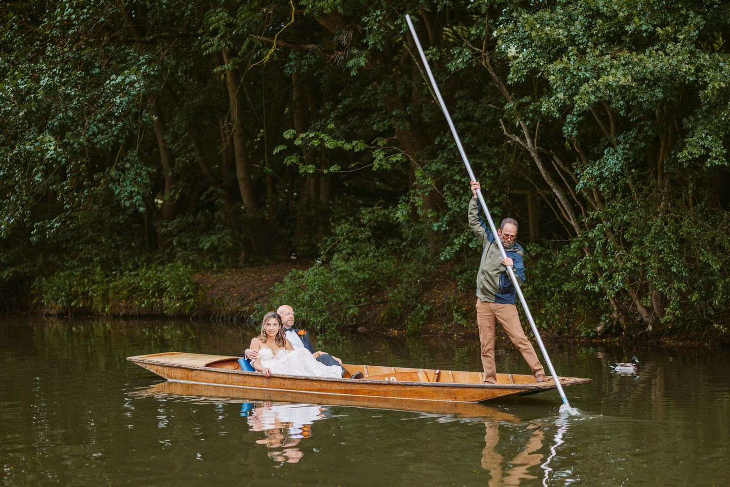 A wooden canoe glides through tranquil waters surrounded by lush green trees on a peaceful summer day.