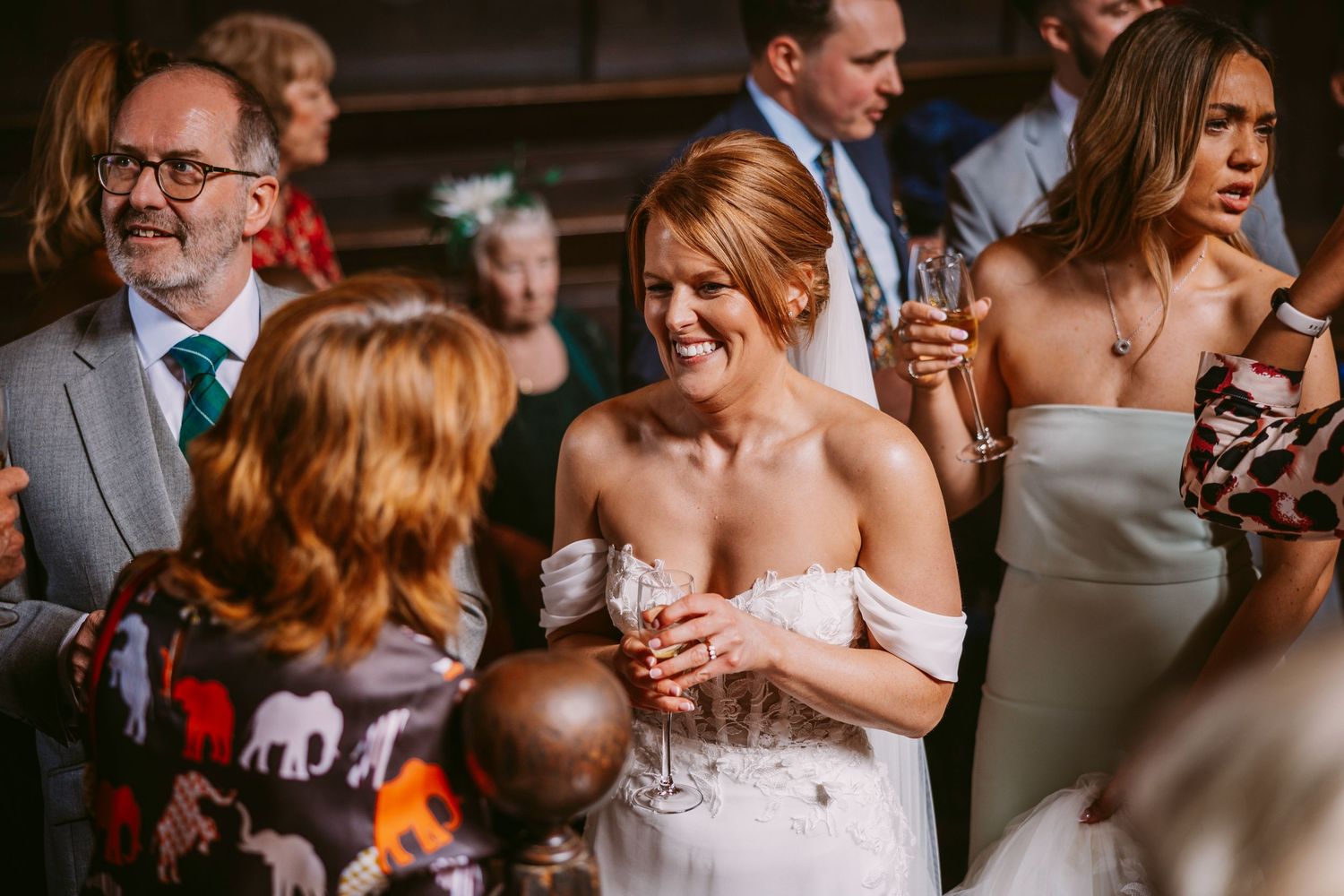 A candid moment at a wedding reception shows guests laughing and enjoying themselves in warm lighting.