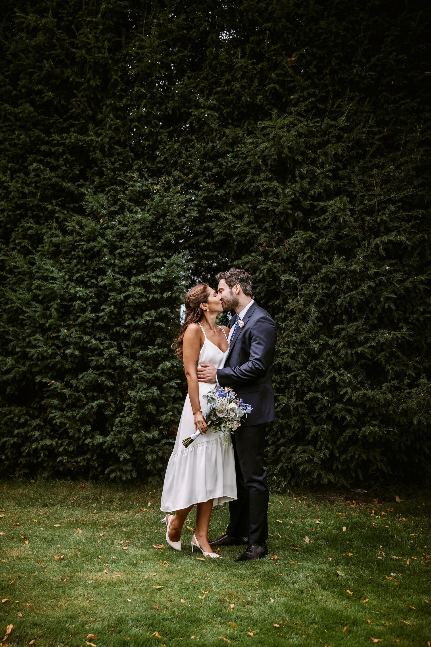 A romantic moment captured between a couple on a green lawn with hedges in the background.