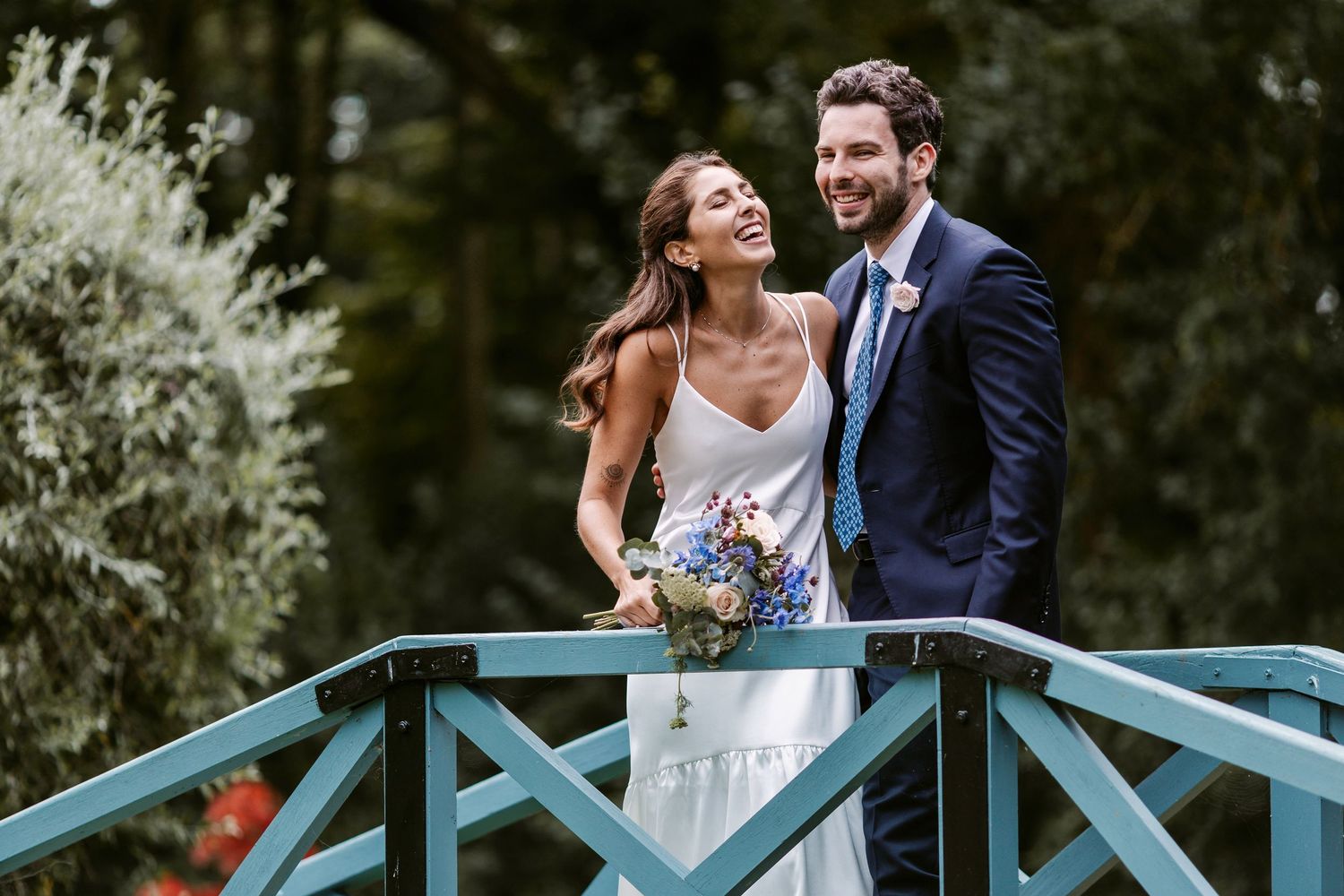 Newlywed couple shares a romantic moment on a turquoise wooden bridge surrounded by lush greenery.