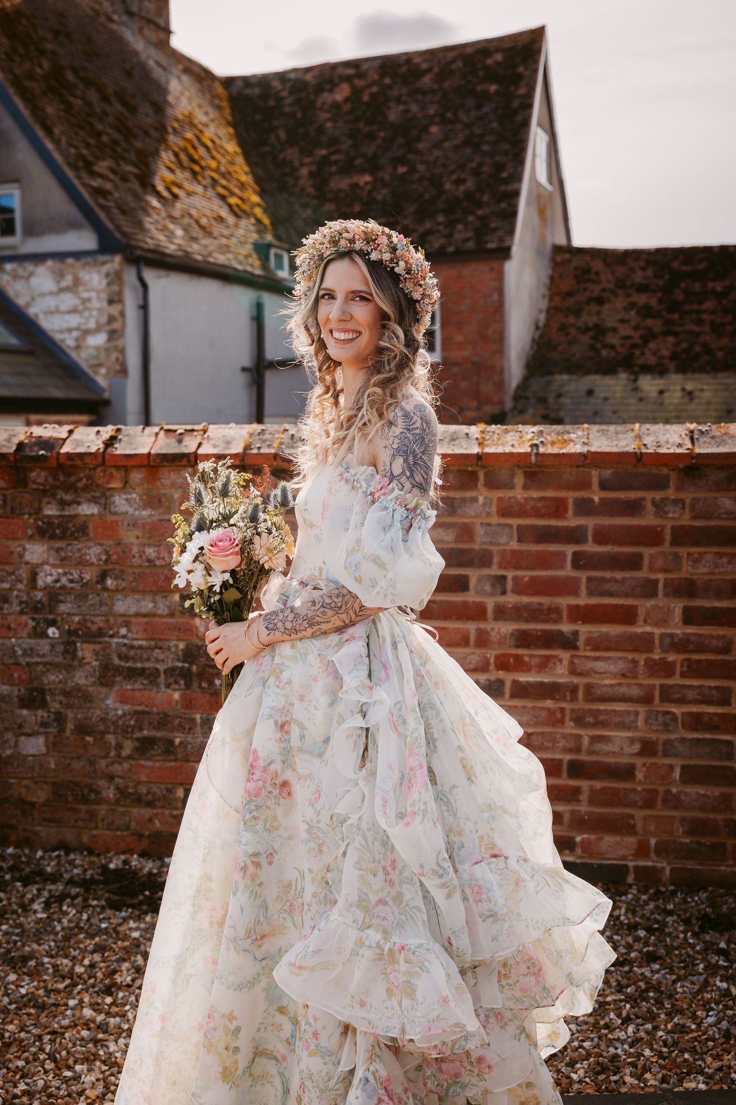 A floral organza wedding dress with ruffled layers and delicate embroidery photographed against rustic brick walls.