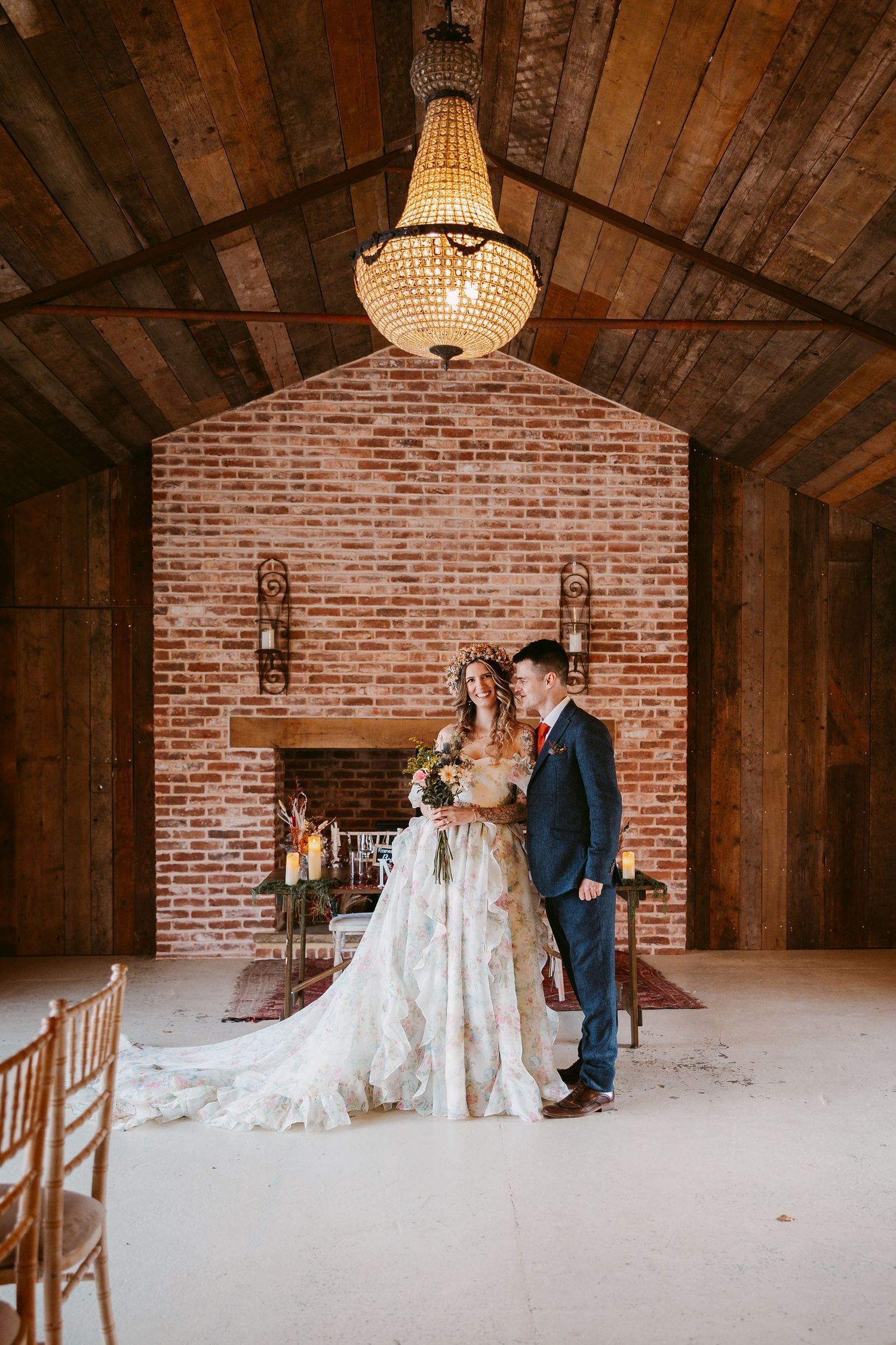 A romantic moment captured in a rustic barn venue with exposed brick walls and crystal chandelier lighting.