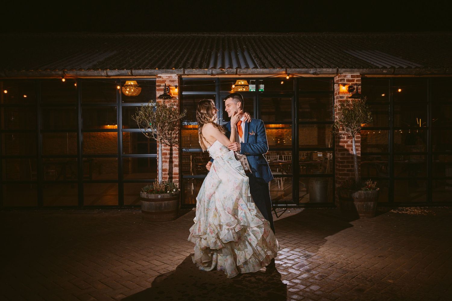 Romantic evening dance poses captured outside an illuminated rustic venue with cobblestone flooring.