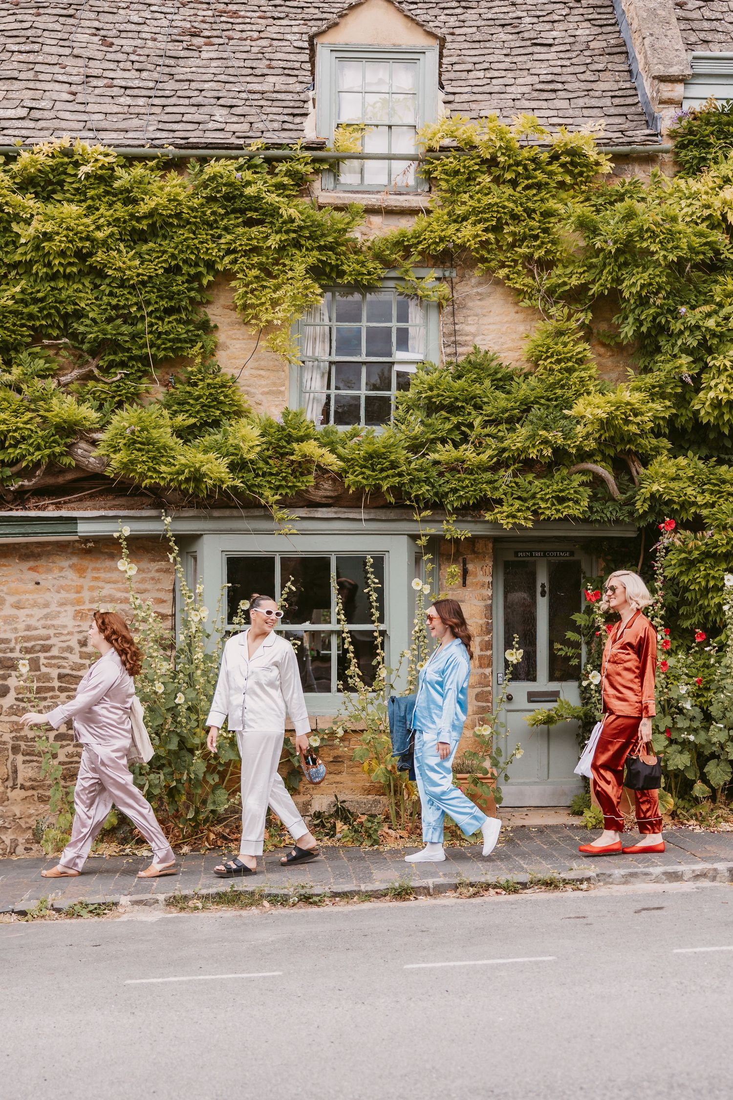 A group of people in colorful outfits walk in a line along a stone building covered in climbing vines.