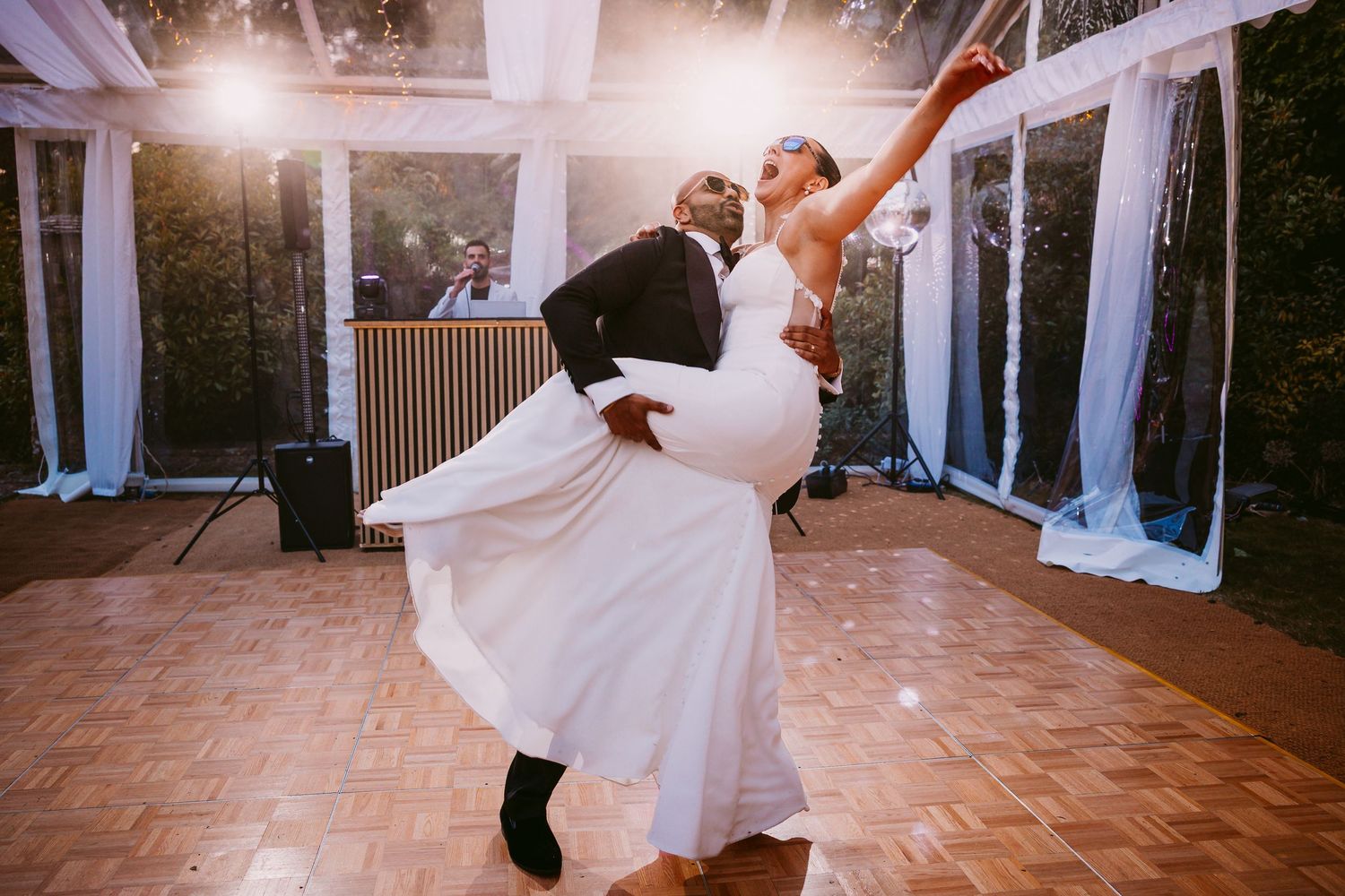 Couple performs elegant dance dip move during romantic first dance at wedding reception with glowing lights.