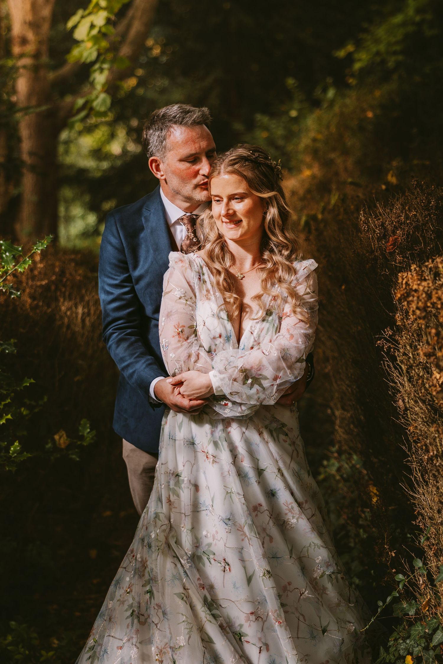A romantic wedding portrait of a couple embracing in a wooded setting during golden hour.