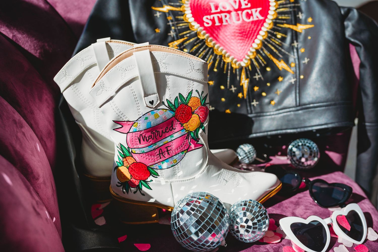 Shiny disco balls and colorful party decorations scattered on pink fabric create a festive celebration setup.