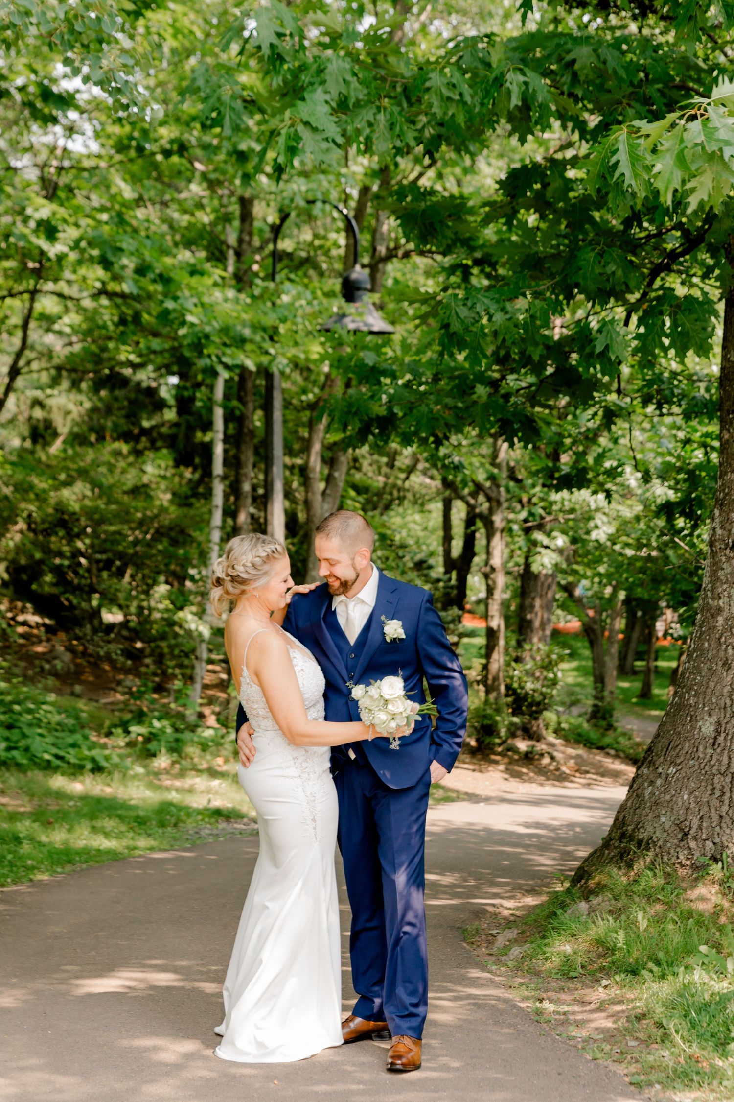 Bride and groom sharing a romantic moment on a sunlit garden path surrounded by lush green trees.