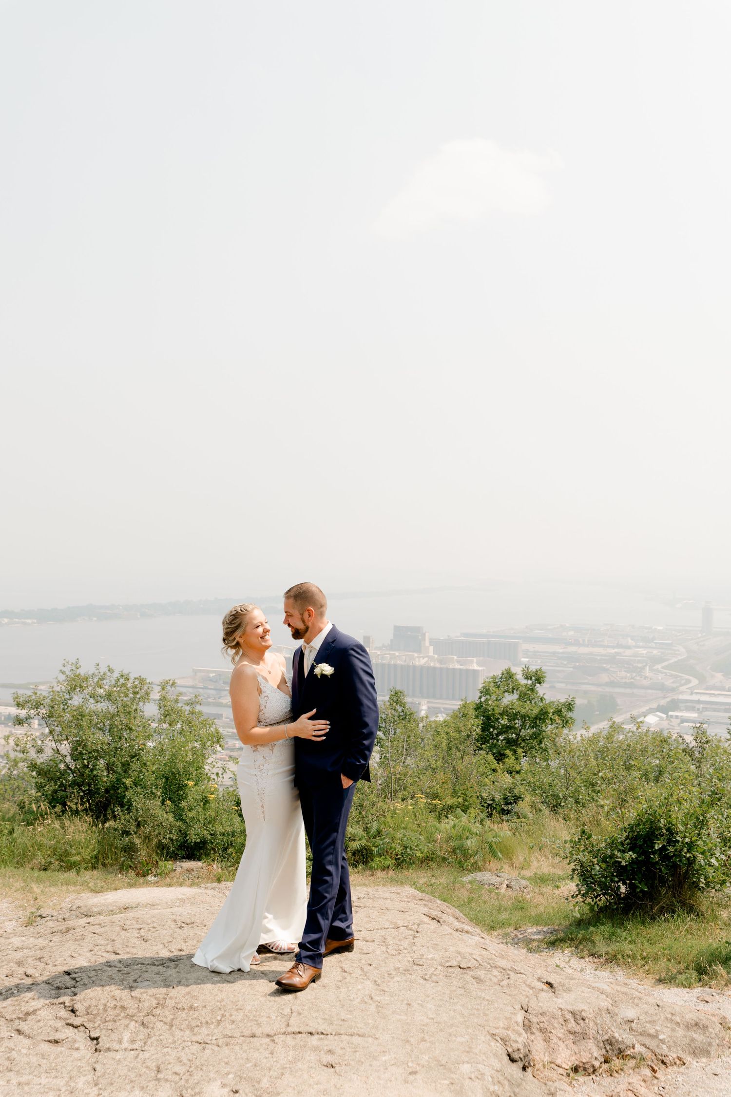 Bride and groom dancing on a rocky overlook with a scenic city and river view on their wedding day.